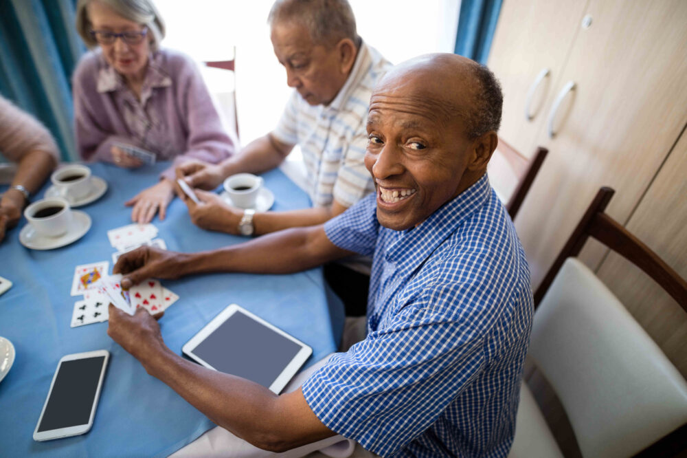 Happy senior man playing cards with friends while having coffee at table