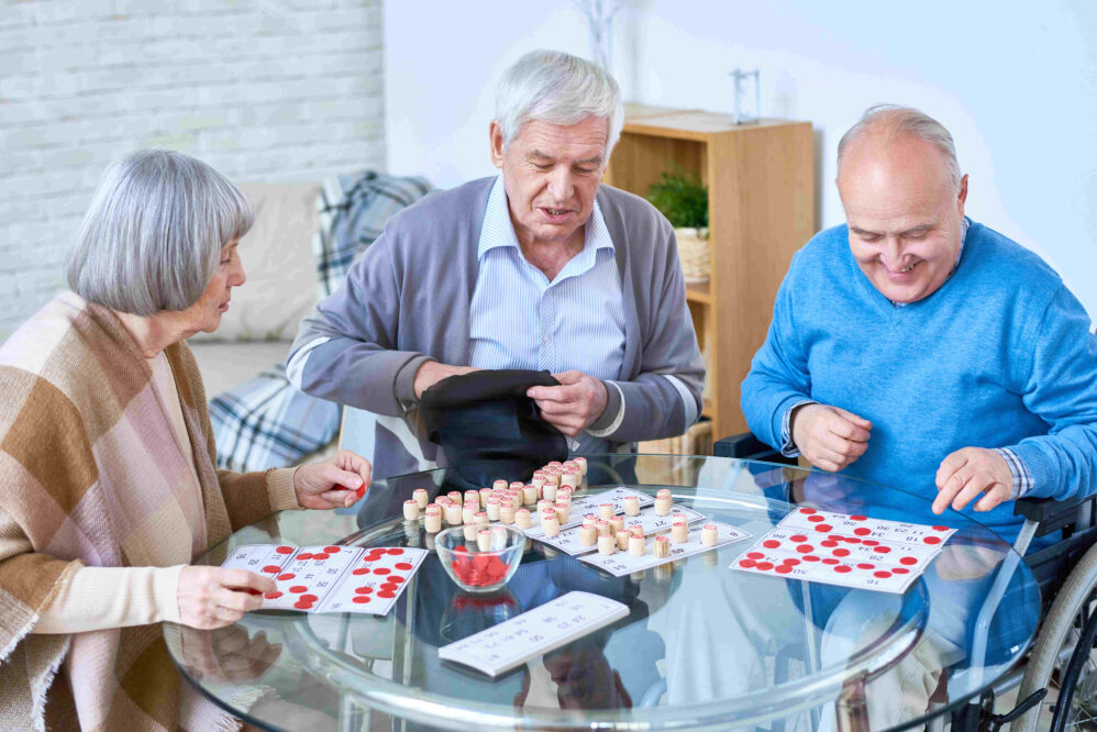 Assisted living. Portrait of senior people playing lotto game sitting at glass table in living room.