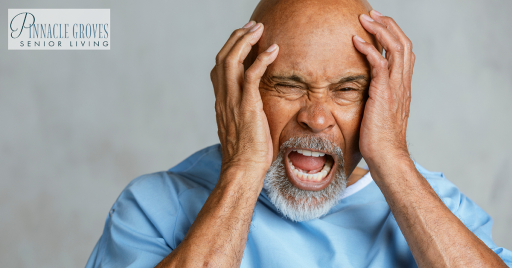 An elderly man in a light blue gown holds his head in distress, appearing frustrated or in pain. This image relates to challenges faced in senior memory care, highlighting the emotional and cognitive struggles that some residents may experience.