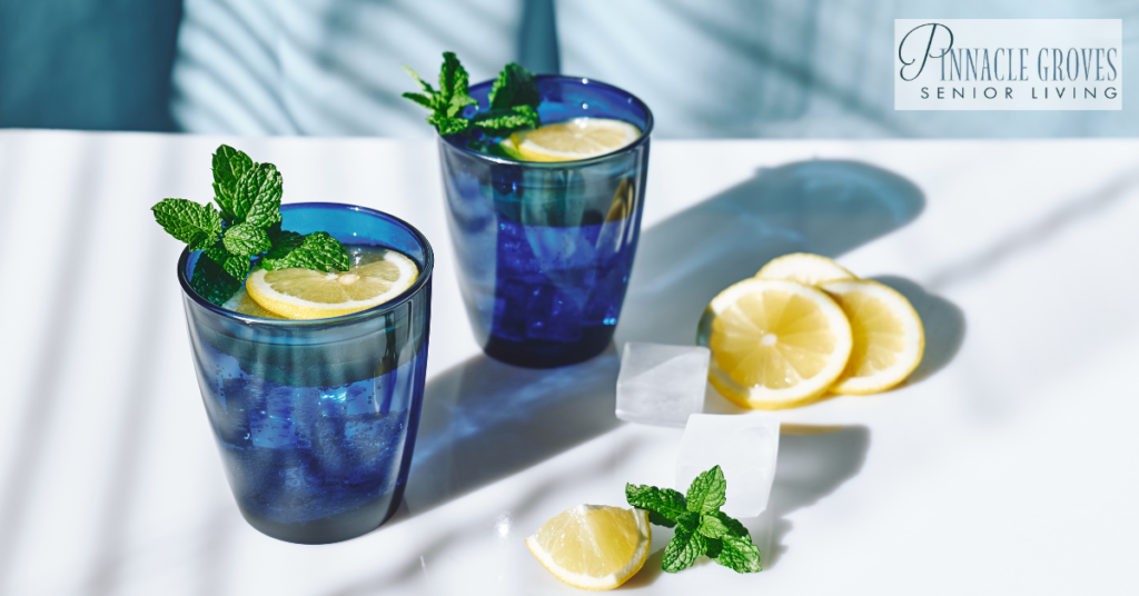 Two glasses of lemon water with mint and ice on a sunny table, symbolizing refreshing hydration options to help preventing dehydration in seniors during warmer months.
