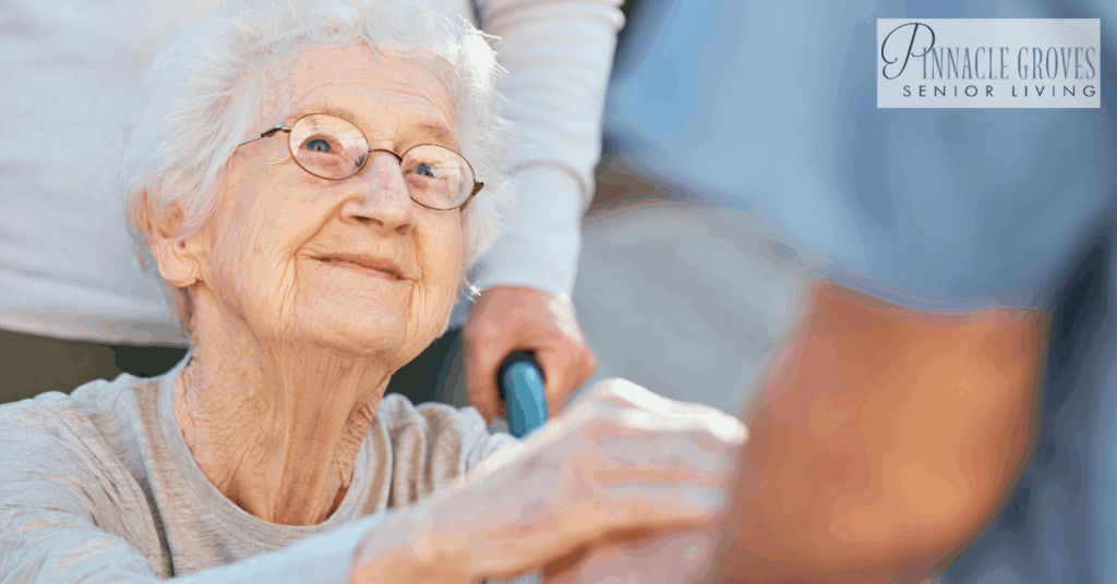 An elderly woman with white hair and glasses smiles warmly while holding hands with a care partner. This image reflects the importance of recognizing the right time for memory care.